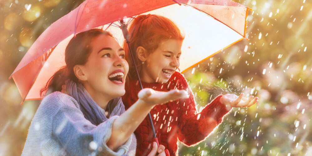 Frau und Kind unter Regenschirm stehend und glücklich